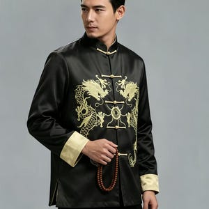 May include: A black long-sleeved jacket featuring a mandarin collar and gold-colored embroidery of two dragons facing each other. The garment includes gold-colored cuffs and traditional frog button closures down the front center.