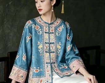 May include: A teal blue jacket featuring intricate floral embroidery in shades of pink, yellow, and white. The garment has a round neckline, three-quarter length sleeves with wide pink cuffs, and a front closure secured by four fabric toggle buttons.
