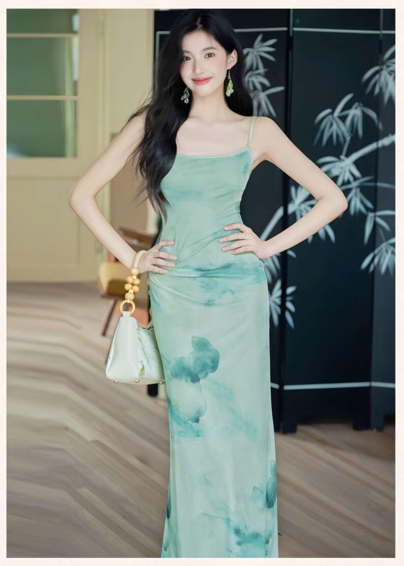 Puede incluir: Un vestido largo verde claro con tirantes finos y un estampado tipo acuarela. El vestido se combina con un bolso blanco con asa dorada. El fondo incluye una pantalla negra con un dise&ntilde;o de bamb&uacute;.