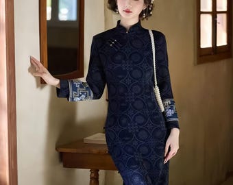 May include: A dark blue long-sleeved cheongsam dress featuring a repeating circular floral pattern, a high mandarin collar, and contrasting light blue and white patterned cuffs. The garment includes a side slit and a white pearl-style shoulder strap.