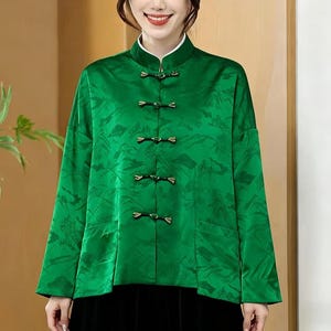 Può includere: Giacca verde brillante con collo alla coreana e maniche lunghe. La giacca presenta un motivo sottile e strutturato ed è chiusa con chiusure a ranocchia decorative. Il colletto ha un bordo bianco. La giacca fa parte di una collezione di abbigliamento.