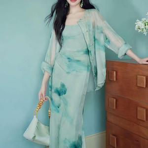 Puede incluir: Conjunto de vestido y chaqueta verde claro, estilo acuarela. El vestido es un vestido largo ajustado con escote cuadrado. La chaqueta transparente tiene un dise&ntilde;o de acuarela a juego y cierres de bot&oacute;n. Un bolso blanco con asas de madera.