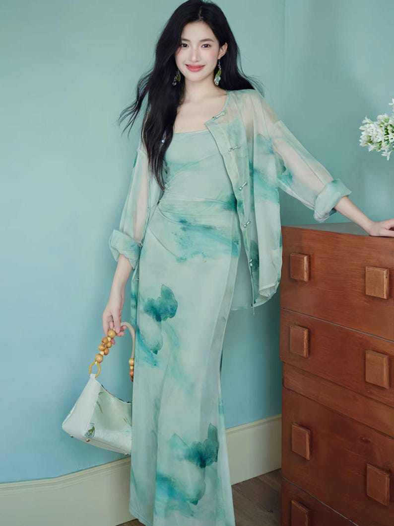 Puede incluir: Conjunto de vestido y chaqueta verde claro, estilo acuarela. El vestido es un vestido largo ajustado con escote cuadrado. La chaqueta transparente tiene un dise&ntilde;o de acuarela a juego y cierres de bot&oacute;n. Un bolso blanco con asas de madera.