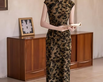 May include: A woman wearing a cap-sleeved, floor-length dress with a floral pattern in black on a tan background. The dress has a mandarin collar and a side slit. She is holding a book and wearing black shoes.