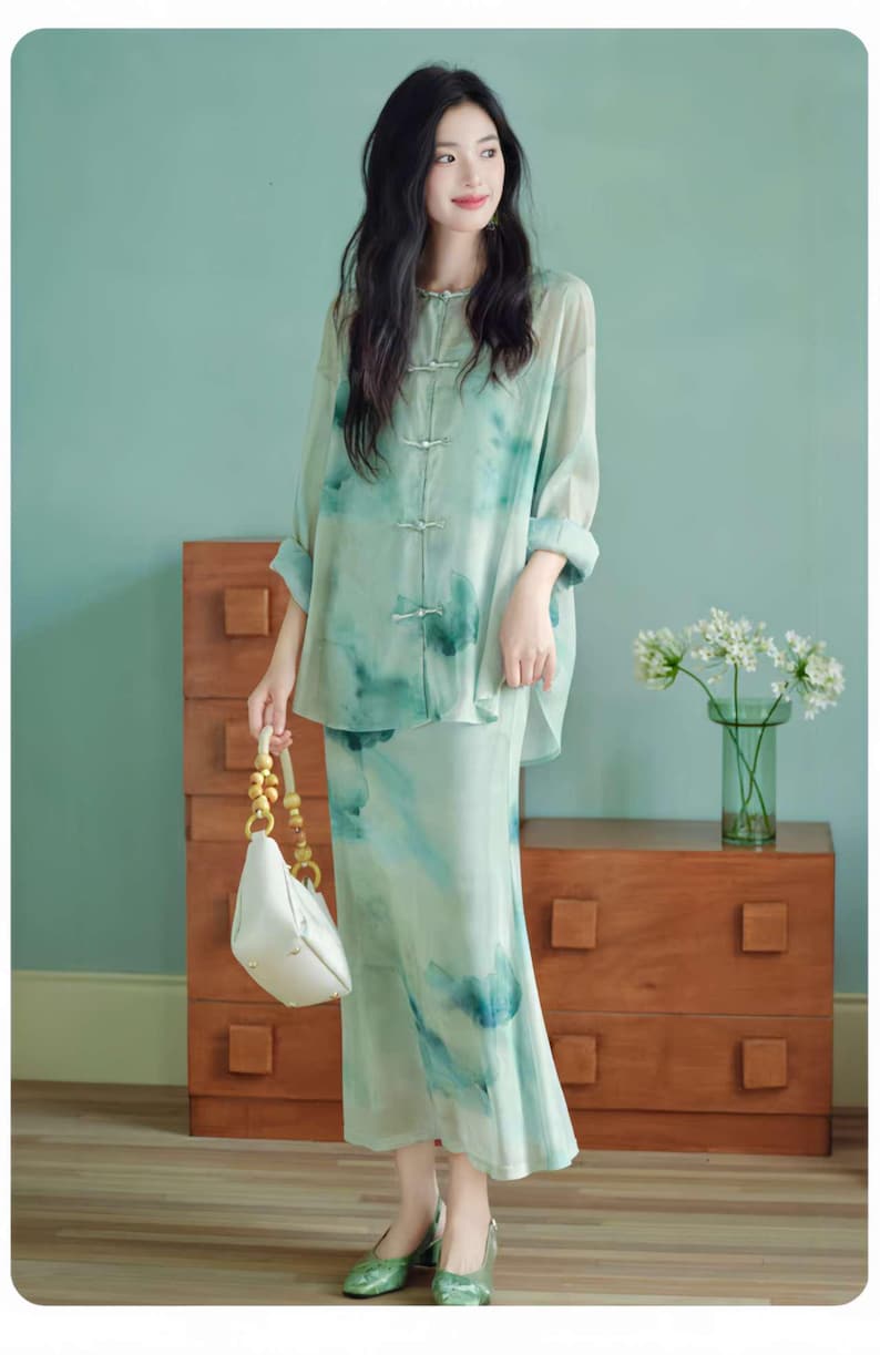 Puede incluir: Un conjunto de dos piezas con una camisa de manga larga con botones y una falda a juego, ambas con un estampado floral de acuarela en verde claro y azul. El conjunto se combina con un bolso blanco y tacones verdes. Un look elegante y con estilo.