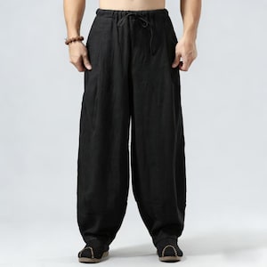 Puede incluir: Pantalones de lino negros con cintura con cordón y perneras anchas. Los pantalones tienen un corte relajado y bolsillos. La tela parece ligera y transpirable, adecuada para climas cálidos. Los pantalones son de color negro sólido.