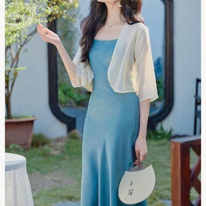 May include: A woman wearing a light blue, floor-length dress with a matching short-sleeved bolero. She is holding a white fan with Asian characters. The words "New fashion" are at the top.