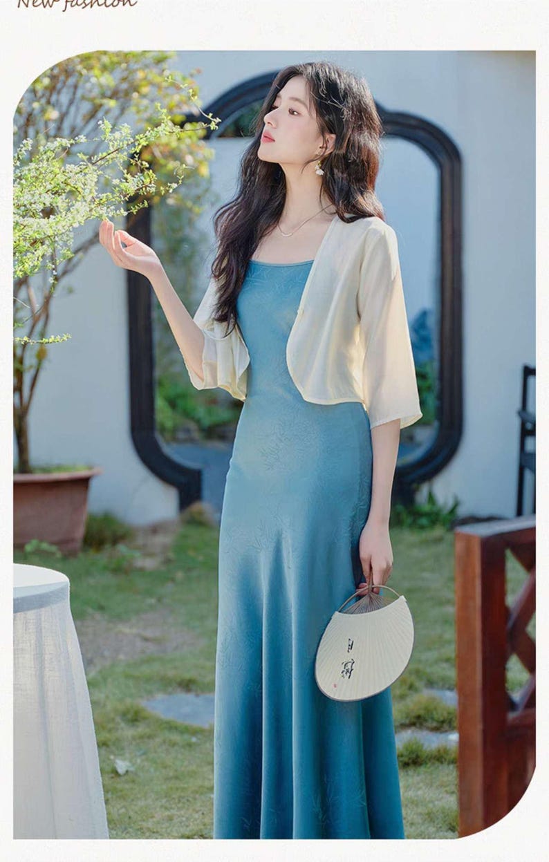 May include: A woman wearing a light blue, floor-length dress with a matching short-sleeved bolero. She is holding a white fan with Asian characters. The words "New fashion" are at the top.