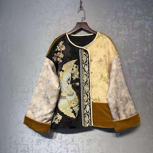 Puede incluir: Chaqueta bicolor en negro y beige. El lado negro presenta bordados dorados de un pájaro y un diseño floral. El lado beige tiene un patrón de paisaje. La chaqueta tiene mangas anchas y un ribete de terciopelo marrón.