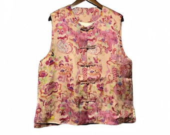 May include: A sleeveless vest with a light pink background and a vibrant floral and mythical creature pattern in shades of pink, purple, and yellow. The vest has a mandarin collar and is fastened with four fabric frog closures.