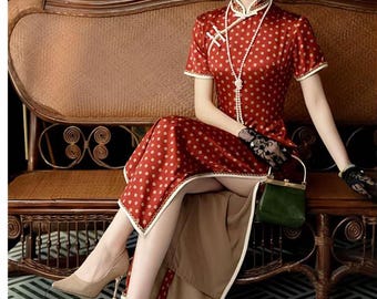 May include: A red, polka-dotted, short-sleeved dress with white trim and a high collar. The dress is paired with beige heels and a small green handbag. The woman is seated on a wooden bench with a patterned background.