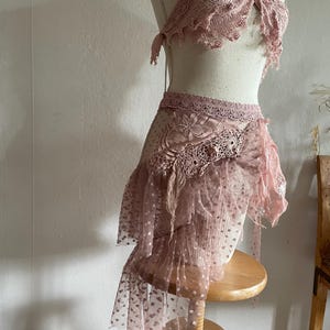 May include: A dusty rose two-piece set featuring a halter-style top with intricate lace detailing and a matching skirt. The skirt is constructed from layers of sheer polka-dot tulle and features a wide lace waistband with floral embroidery.