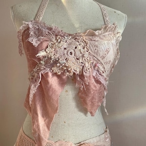 Puede incluir: Un top de encaje rosa con un diseño de ganchillo. El top está hecho de tela delicada y tiene una estética vintage.
