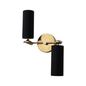 May include: A gold wall sconce with two black cylindrical shades. The sconce has a swivel arm that allows the shades to be adjusted.