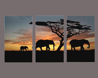 Könnte beinhalten: Ein dreiteiliger Leinwanddruck mit Silhouetten von Elefanten und einem Baum vor einem Sonnenuntergang. Das Kunstwerk zeigt eine afrikanische Savannenszene mit warmen Orange-, Gelb- und Blautönen. Die Elefanten laufen über den Horizont.