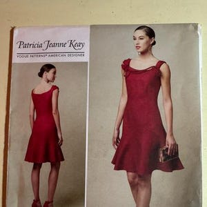 May include: A Vogue Patterns sewing pattern envelope for a Patricia Jeanne Keay design, labeled V1542. The front shows a deep red knee-length dress with a scoop neckline and flared hem, displayed from both front and back views on a model.