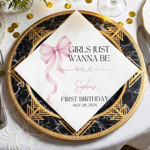 May include: A white square paper napkin featuring a watercolor pink bow and black text that reads GIRLS JUST WANNA BE one, Sophia's FIRST BIRTHDAY, MAY 20, 202X. The napkin is placed on a black and gold decorative plate with a geometric pattern.