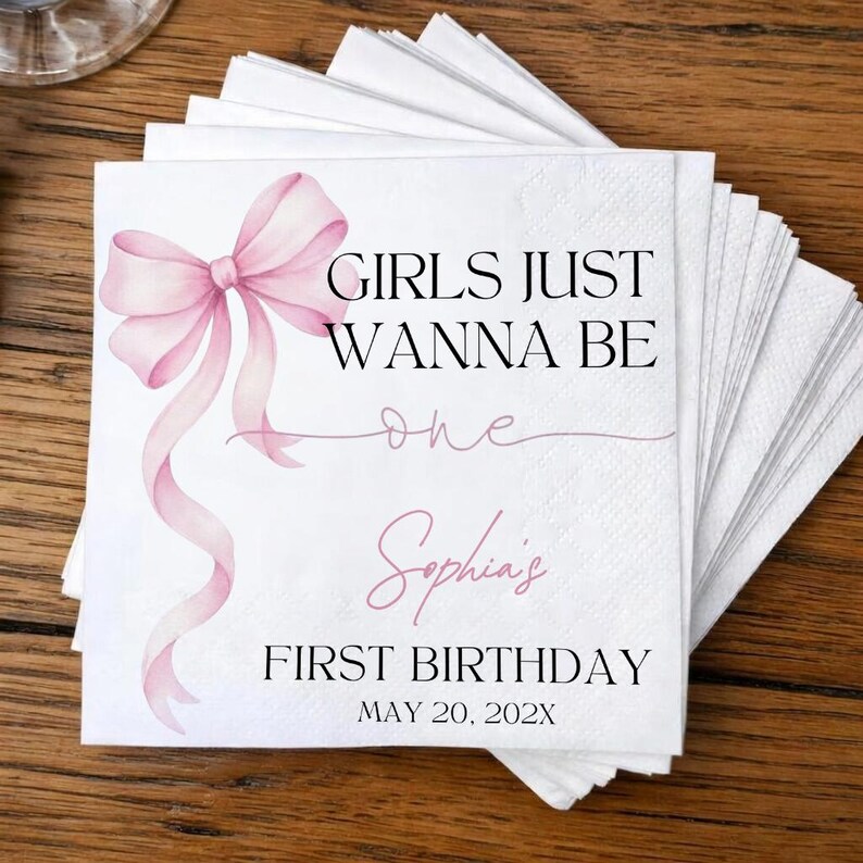 May include: A stack of white paper napkins featuring a watercolor pink bow on the left side. The text reads GIRLS JUST WANNA BE one, Sophia's, FIRST BIRTHDAY, and MAY 20, 202X in black and pink script and serif fonts on the front napkin surface.
