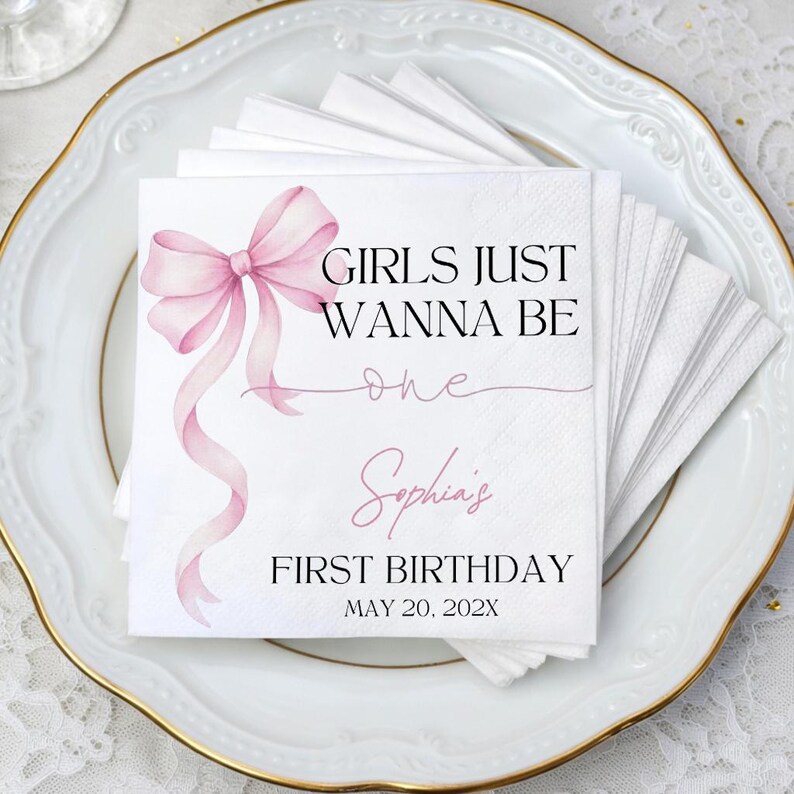 May include: A stack of white paper napkins featuring a watercolor illustration of a light pink ribbon bow. The text reads: GIRLS JUST WANNA BE one, Sophia's FIRST BIRTHDAY, MAY 20, 202X. The napkins are square with a textured border and printed design.