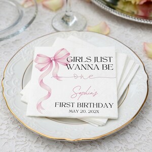 May include: A white paper napkin featuring a pink watercolor bow graphic and black text that reads GIRLS JUST WANNA BE one, Sophia's FIRST BIRTHDAY, and MAY 20, 202X. The design includes a thin pink script line and elegant typography.