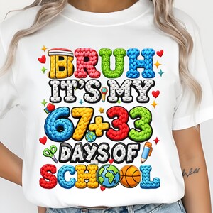 Puede incluir: Camiseta blanca con un gráfico colorido que dice "BRUH IT'S MY 67+33 DAYS OF SCHOOL". El diseño incluye corazones, estrellas, un globo terráqueo, una pelota de baloncesto y un lápiz.