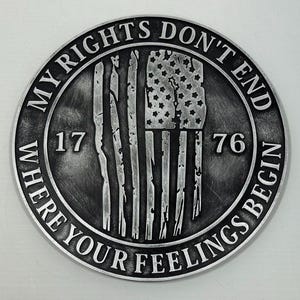 May include: A circular, silver-toned coin featuring the text "MY RIGHTS DON'T END WHERE YOUR FEELINGS BEGIN" around the edge. The centre displays a distressed American flag design and the numbers "1776".