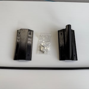 May include: A set of black metal hardware components, including two brackets, a long rod, and a small bag of screws. The items are arranged on a white surface, likely for installation.