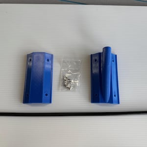 May include: An overhead shot shows a set of blue plastic components, including two rectangular brackets, a black rod, and a small bag of screws. The brackets have pre-drilled holes for mounting. The items are arranged on a white surface.