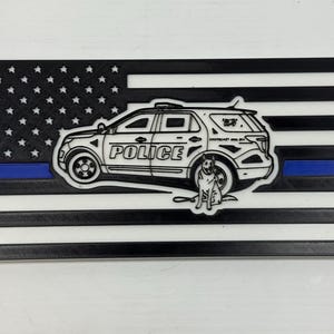 May include: A black and white flag design with a blue stripe, featuring a police SUV and a dog. The word "POLICE" is on the vehicle. The flag has a 3D printed appearance.