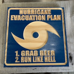 May include: Square wooden sign with a blue painted background and a carved hurricane symbol. The text reads "HURRICANE EVACUATION PLAN" above the symbol, and "1. GRAB BEER 2. RUN LIKE HELL" below. The sign has a natural wood border.