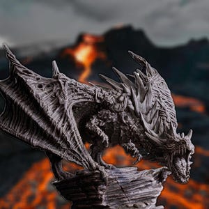 Puede incluir: Una detallada escultura de dragón gris con alas y escamas texturizadas, posada sobre una base rocosa. El dragón se encuentra sobre un fondo borroso de un paisaje volcánico con lava fluyendo, creando un tema de fantasía.