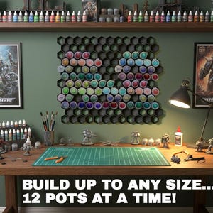 May include: A hobbyist's workspace with a wooden table, miniature figures, paint bottles, and tools. The wall displays framed Warhammer art, paint storage, and the text "BUILD UP TO ANY SIZE... 12 POTS AT A TIME!"
