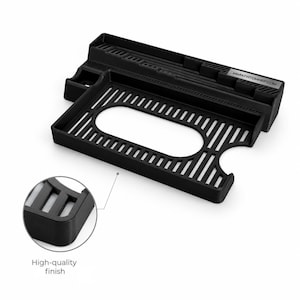 May include: A black 3D-printed organizer tray featuring a rectangular base with a central oval cutout and a slatted grid pattern. The back section includes a raised ledge with vertical slots and a small rectangular plate labeled WWW.FATDWARF.COM.