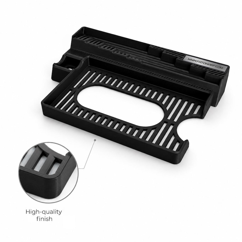 May include: A black 3D-printed organizer tray featuring a rectangular base with a central oval cutout and a slatted grid pattern. The back section includes a raised ledge with vertical slots and a small rectangular plate labeled WWW.FATDWARF.COM.