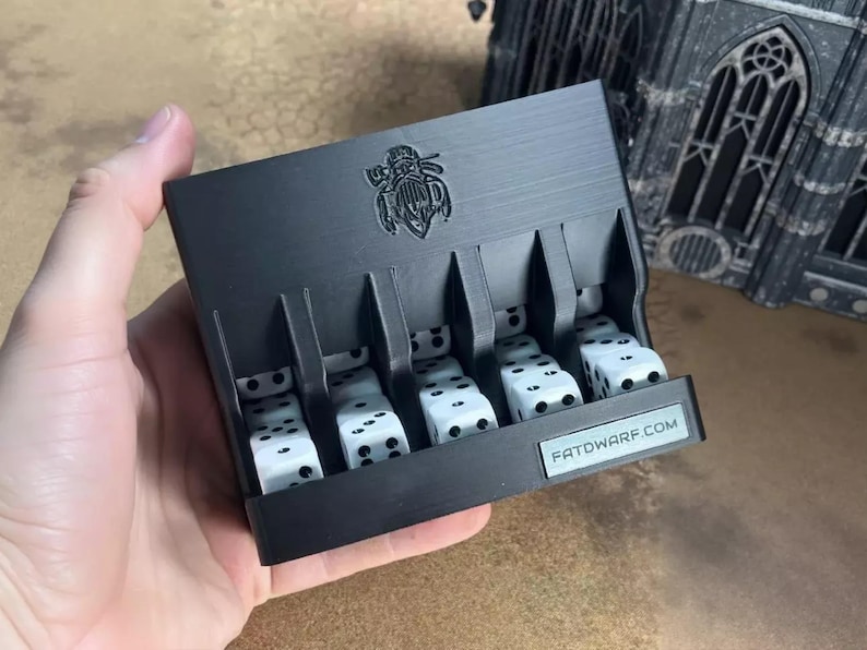 A hand is holding a black tray with six white dice on it, with a logo on the tray. In the background, there is a large, ornate building.