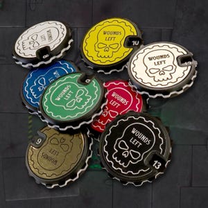 May include: A set of eight round, multi-colored, plastic wound counters with a skull graphic and the text "Wounds Left". The counters are numbered 8, 9, 10, 12, and 13.