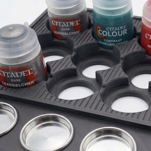 May include: A black paint bottle holder with multiple circular slots for paint bottles and small metal mixing pots. The holder contains Citadel brand paint bottles in various colors, including Leadbelcher and Akhelian Green.