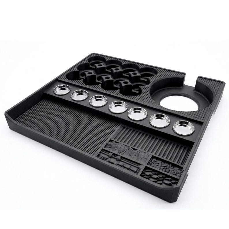 May include: A black, multi-compartment tray with various shaped recesses. It features a series of small, round, silver-colored metal containers and several cup-shaped holders. The tray has a textured surface and a large circular opening on the side.