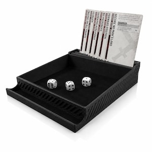 Peut inclure: Un plateau à dés noir texturé avec un intérieur doublé de feutre contenant trois dés blancs à six faces. Un porte-cartes vertical à l'arrière affiche plusieurs cartes de jeu avec du texte dont SECURE NO MAN'S LAND, FORWARD POSITION et ENGAGE ON ALL FRURTS.
