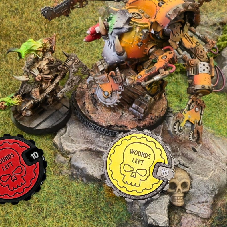 May include: Two yellow and red plastic tokens with a skull and the words "Wounds Left" and a number "10". The tokens are used for a tabletop game.