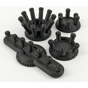 Puede incluir: Cuatro objetos negros impresos en 3D están dispuestos sobre una superficie blanca. Los objetos incluyen tres bases circulares con postes verticales y una base alargada con postes. Los postes tienen un diseño floral.