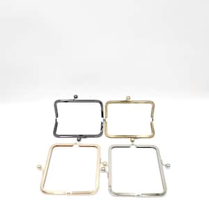 May include: Four metal purse frames in various finishes: black, gold, rose gold, and silver. Each frame has a rectangular shape with a clasp closure. The frames are shown against a white backdrop.
