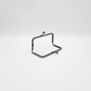May include: A gunmetal-coloured purse frame with a rectangular opening and rounded corners. The frame has a ball clasp on the top and bottom, and is open, showing the interior space. The frame is made of metal.