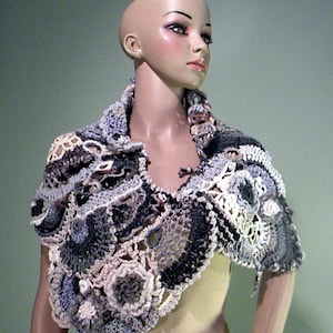 May include: A crocheted shawl in shades of gray, white, and black with a delicate lace pattern. The shawl is draped over a mannequin's shoulders.