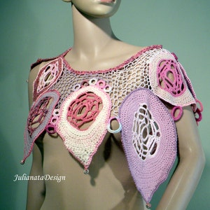 May include: A crocheted pink and white collar with a delicate, lacy design. The collar features a variety of circular and oval shapes, creating a unique and intricate pattern.