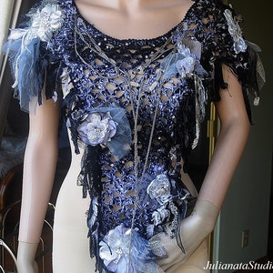 May include: A crocheted top in a blue and black colour scheme. The top is decorated with silver chains, beads, and flowers. The top has a loose, flowing fit.
