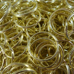 May include: A large pile of gold-coloured metal key rings. The key rings are all the same size and shape, and they are arranged in a random pattern.