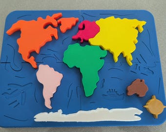 Può includere: Un tappetino da puzzle in schiuma blu con un contorno di mappa del mondo. I continenti sono pezzi separati di diversi colori: Nord America (arancione), Sud America (rosa), Europa (rosso), Asia (giallo), Africa (verde), Australia (marrone) e Antartide (bianco).