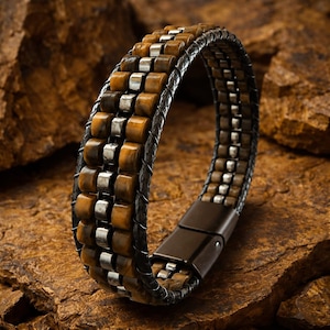 Könnte beinhalten: Ein mehrreihiges Armband mit braunen Tigeraugenperlen und silberfarbenen Metallzwischenstücken, zusammengehalten durch dunkle geflochtene Lederbänder und einen rechteckigen magnetischen Verschluss aus dunklem Metall.