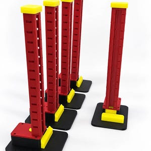May include: Five vertical red towers with yellow square caps and yellow rectangular base accents, each mounted on a flat black square platform. The towers feature a series of evenly spaced horizontal slots along their length, creating a structured design.